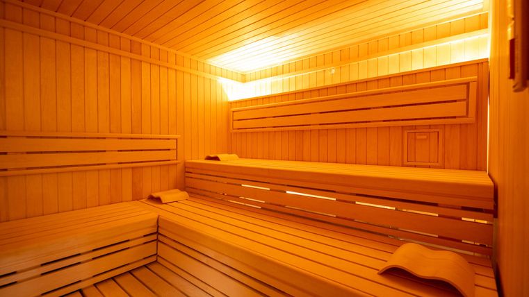 Eine holzverkleidete Sauna mit warmem Licht. Bänke und Ablagen bieten Platz zum Entspannen.
