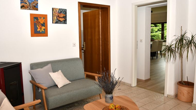 Ein gemütliches Wohnzimmer mit einem grauen Sofa und einem Holztisch. An der Wand hängen Kunstwerke und eine Pflanze steht in einer Ecke.