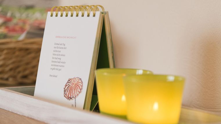 Ein kleiner Tisch mit einem aufgestellten Notizblock und zwei gelben Teelichtern. Der Notizblock zeigt ein süßes Design mit einer pinken Süßigkeit.