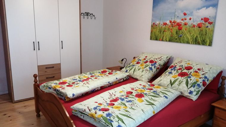 Ein gemütliches Schlafzimmer mit einem Doppelbett und bunten Blumenbettwäsche. An der Wand hängt ein Bild von blühenden Mohnfeldern.