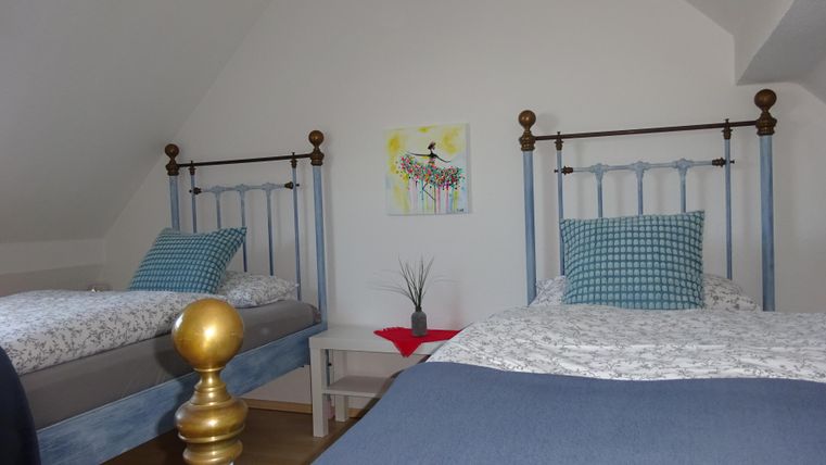 Ein gemütliches Schlafzimmer mit zwei Betten und hellen Wänden. Ein kleines Bild hängt an der Wand, und es gibt eine Pflanze auf dem Tisch.