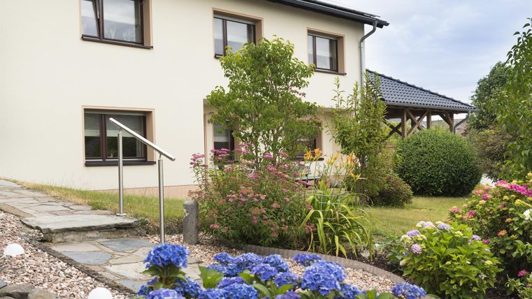 Ein modernes Haus mit einem schönen Garten und bunten Blumen. Der Eingangsbereich ist einladend, umgeben von grünen Pflanzen.