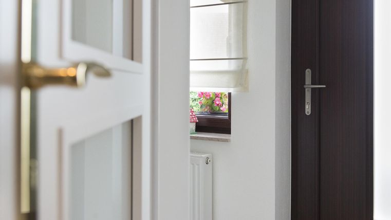 Ein heller Flur mit einer Tür und einem Fenster. Durch das Fenster sieht man bunte Blumen.