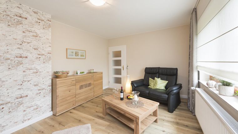 Ein gemütliches Wohnzimmer mit einem schwarzen Sessel und einem Holztisch. Die Wände sind hell gestrichen und es gibt einen dekorativen Steinakzent.