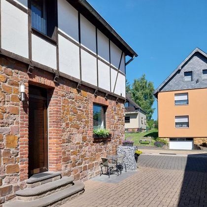 Ein charmantes, altes Gebäude aus Stein steht neben einem modernen Haus. Der Innenhof ist gepflastert und lädt zum Verweilen ein.