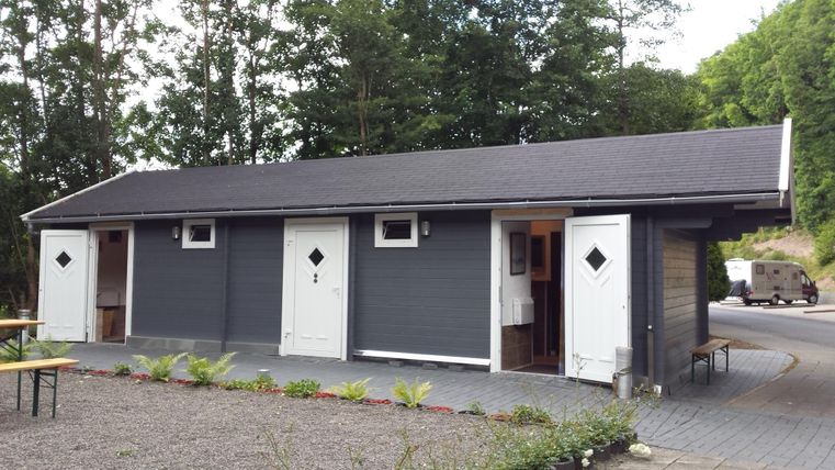 Un bâtiment moderne avec une façade grise et plusieurs entrées. Il se trouve dans un environnement calme avec des arbres en arrière-plan.