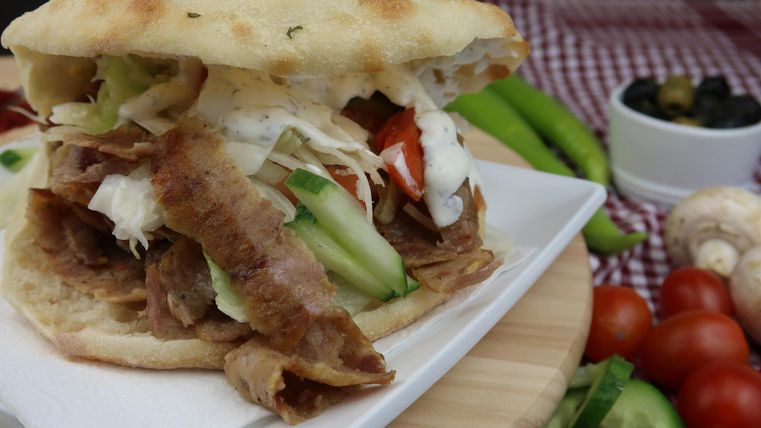 A freshly prepared sandwich with meat, salad, and vegetables in a bread. In the background, various fresh ingredients can be seen.