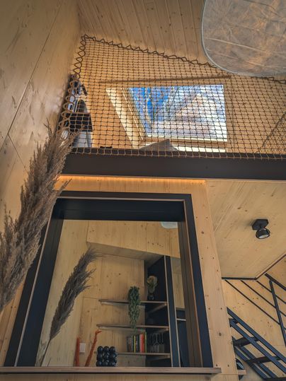 Ein modernes, helles Wohnzimmer mit Holzverkleidung und einem schönen Oberlicht. Eine elegante Treppe führt in eine obere Etage, die durch ein Netzwerk aus Seilen gesichert ist.
