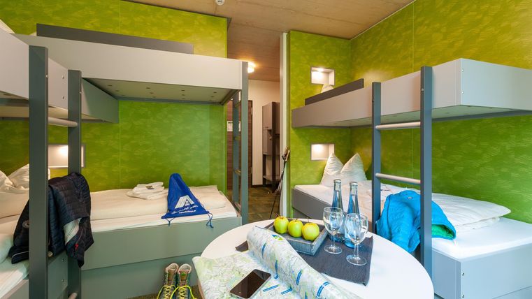 Ein modernes Schlafzimmer mit Etagenbetten und einer leuchtend grünen Wand. Auf dem Tisch liegen Getränke und Sportausrüstung.