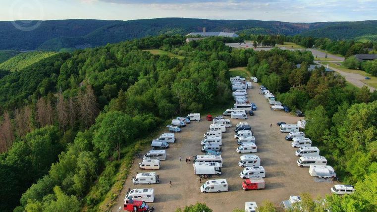 Ein großer Campingplatz auf einem Hügel, umgeben von Bäumen und Bergen. Zahlreiche Wohnmobile sind auf gravelboden geparkt.