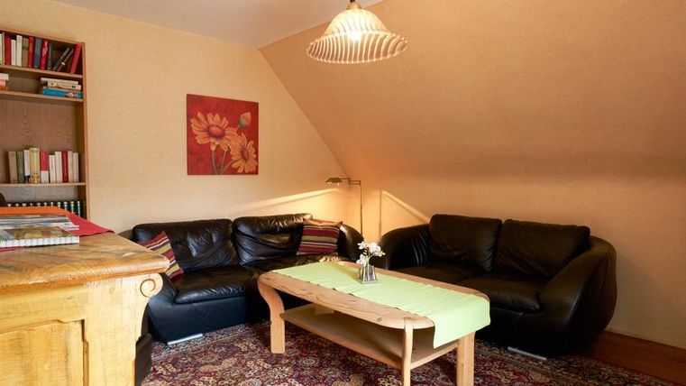 Ein gemütliches Wohnzimmer mit schwarzen Ledersofas und einem Holztisch. An der Wand hängt ein Gemälde mit Blumenmotiven.