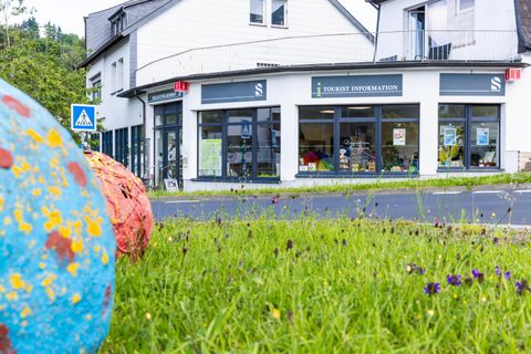 Een informatiepunt voor toeristen met grote ramen en een uitnodigende ingang. Op de voorgrond zijn kleurrijke, decoratieve ballen op een groene weide te zien.