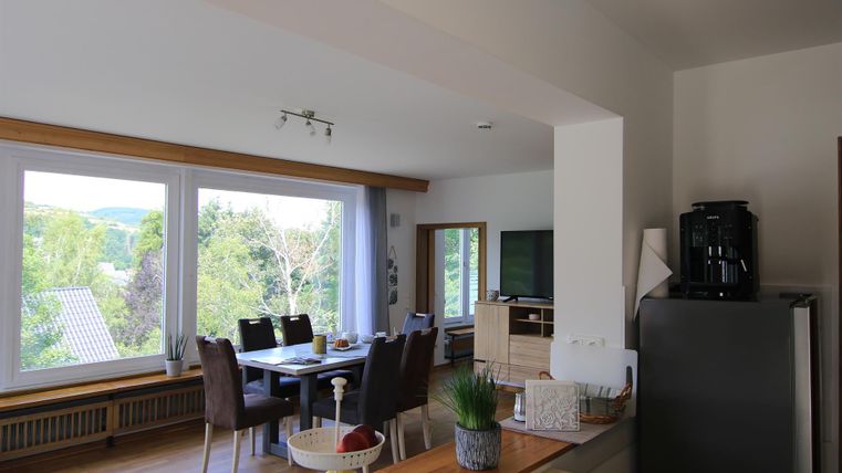 Eine helle Küche mit einem Esstisch und gemütlichen Stühlen. Große Fenster bieten einen Blick auf die grüne Umgebung.