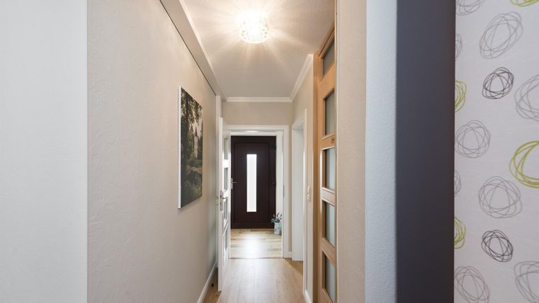 Ein heller Flur mit Holzfußboden und modernen Wänden. Am Ende des Flurs befindet sich eine Eingangstür.