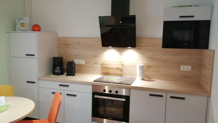 Eine moderne Küche mit einem Herd, einer Dunstabzugshaube und einem Kühlschrank. Der Holz-Look und die hellen Farben schaffen eine freundliche Atmosphäre.