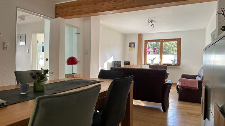 Ein helles und modernes Wohnzimmer mit Holzdetails. Der Raum ist gemütlich eingerichtet und hat große Fenster, die viel Licht hereinlassen.