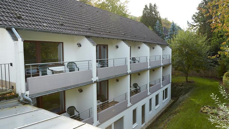 Ein modernes Wohngebäude mit mehreren Balkonen. Der Blick zeigt einen ruhigen Gartenbereich im Hintergrund.