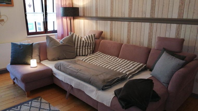 Ein gemütliches Wohnzimmer mit einem bequemen, rosa Sofa und vielen Kissen. Der Raum hat einen warmen, einladenden Stil mit Holzboden und einer ruhigen Atmosphäre.