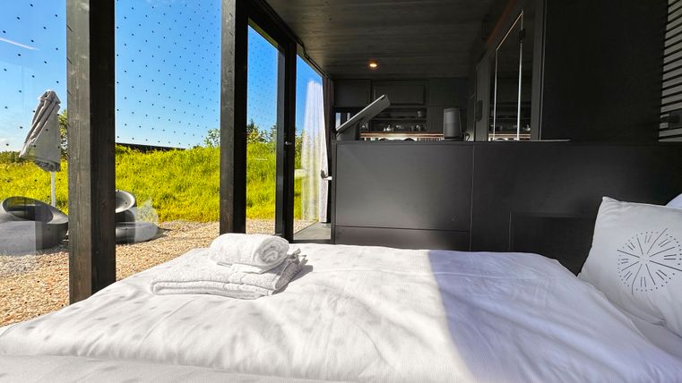 Ein modernes Schlafzimmer mit einem großen Bett und Blick auf die Natur. Große Fenster lassen viel Licht herein und bieten einen schönen Ausblick.