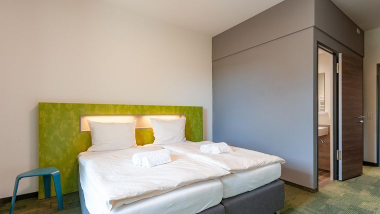 Ein modernes Hotelzimmer mit zwei Betten und frischen weißen Bettwäsche. Der Raum hat eine helle, einladende Atmosphäre und Zugang zum Badezimmer.