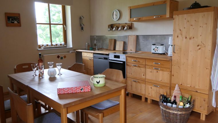 Eine gemütliche Küche mit Holzmöbeln und einem großen Esstisch. Das Raumdesign ist hell und einladend, mit Fenstern, die Tageslicht hereinlassen.