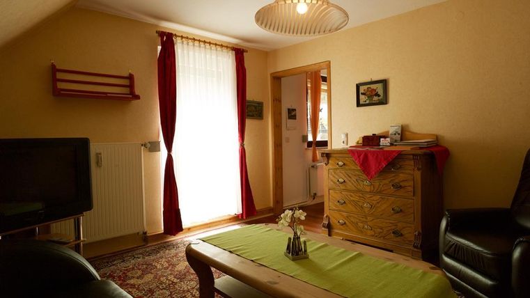 Ein gemütlicher Wohnraum mit einem Tisch und einem Fernseher. Das Licht fällt durch die Vorhänge und es gibt eine interessante Möbelanordnung.