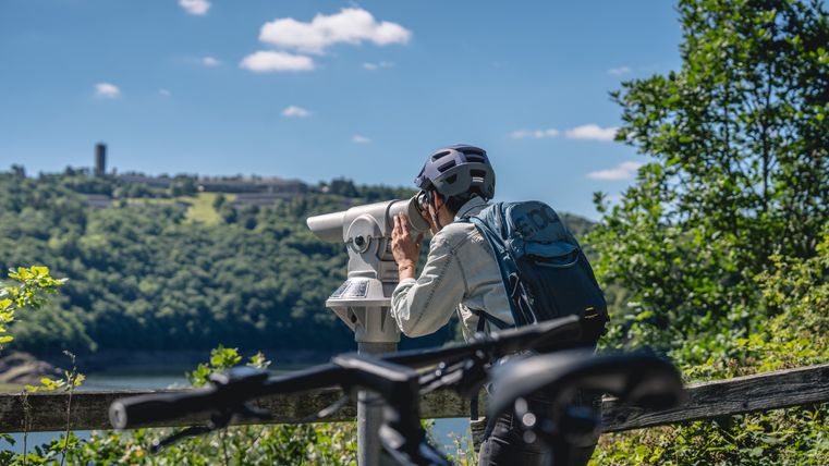 Person mit Helm schaut durch ein Fernglas auf einer Vogelbeobachtungsstation, im Hintergrund Vogelsang IP.