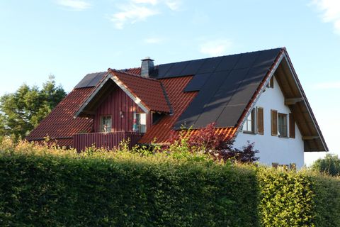 Ein charmantes Haus mit rotem und weißen Anstrich sowie einem modernen Dach. Es ist von einer grünen Hecke umgeben und steht unter einem klaren Himmel.