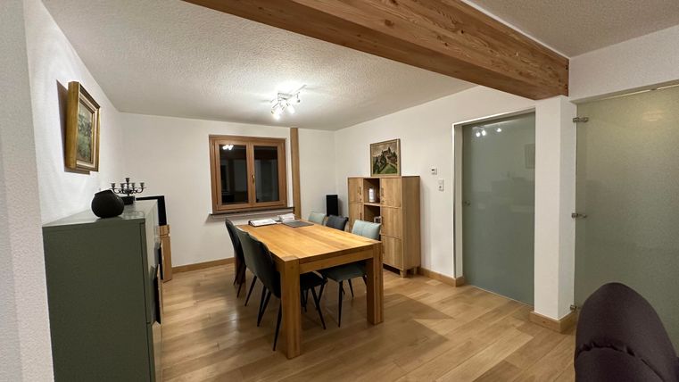 Ein modernes Esszimmer mit einem großen Holztisch und Stühlen. Die Wände sind hell und es gibt ein Fenster, das natürliches Licht hereinlässt.