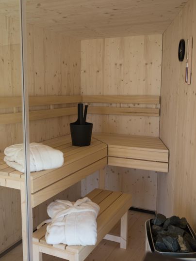Eine moderne Sauna mit Holzverkleidung und zwei Bänken. Im Raum befinden sich Handtücher und ein schwarzer Eimer.
