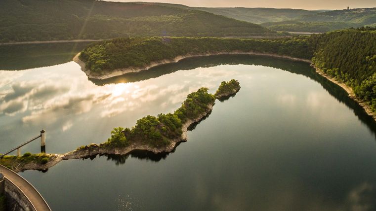Un paysage lacustre calme avec des collines douces et un peu de verdure. Le ciel se reflète clairement dans l'eau.