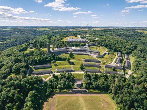 Un paysage impressionnant avec des bâtiments historiques, entouré de collines boisées. Le ciel est dégagé et l'atmosphère est paisible.