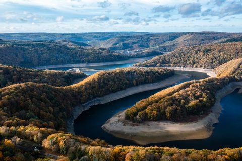 Eine malerische Landschaft mit sanften Hügeln und einem geschlängelten Fluss. Die Bäume leuchten in herbstlichen Farben unter einem klaren Himmel.