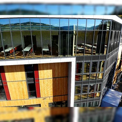 Ein modernes Gebäude mit großen Fenstern und einer stilvollen Holzverkleidung. Im Inneren sind einladende Arbeitsplätze zu sehen.