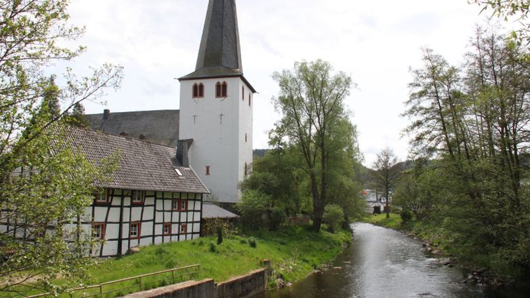 Kirche in Olef am Fluss mit Fachwerkhaus im Vordergrund.