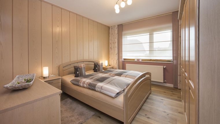 Ein gemütliches Schlafzimmer mit Holzvertäfelung und einem Doppelbett. Der Raum hat große Fenster und sanfte Beleuchtung.