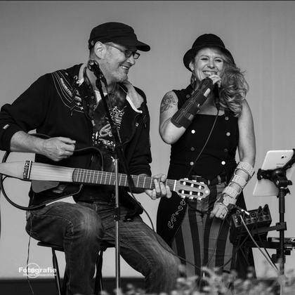 Ein Duo tritt auf einer Bühne auf. Die Musikerin singt, während der Musiker Gitarre spielt.
