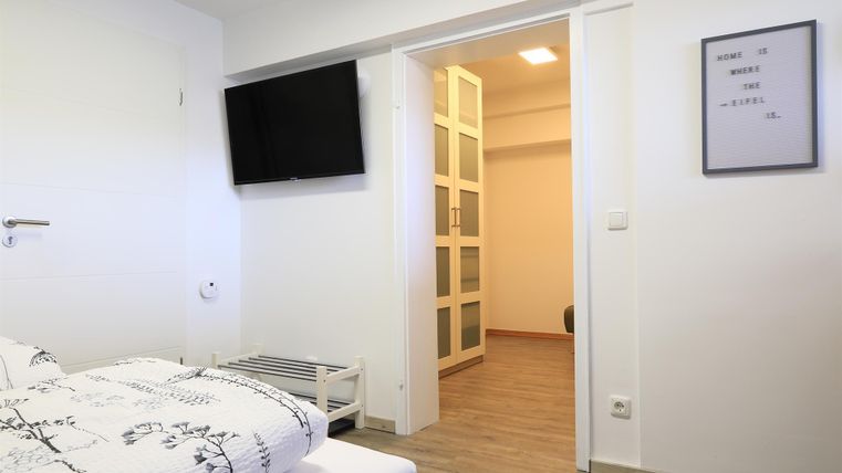 Ein modernes Schlafzimmer mit einem Doppelbett und einem Fernseher an der Wand. Der Raum hat einen hellen Boden und einen Schrank im Hintergrund.