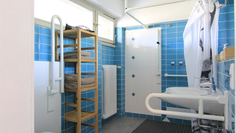 Ein helles Badezimmer mit blauen Fliesen und einem modernen Duschbereich. Zur Ausstattung gehören ein Handtuchregal und ein Waschbecken mit Haltegriffen.