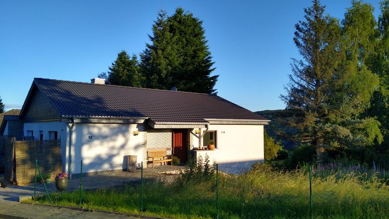 Ein gemütliches Haus mit einem modernen Dach und einem kleinen Eingangsbereich. Umgeben von grünen Bäumen und einem ruhigen Rasen.