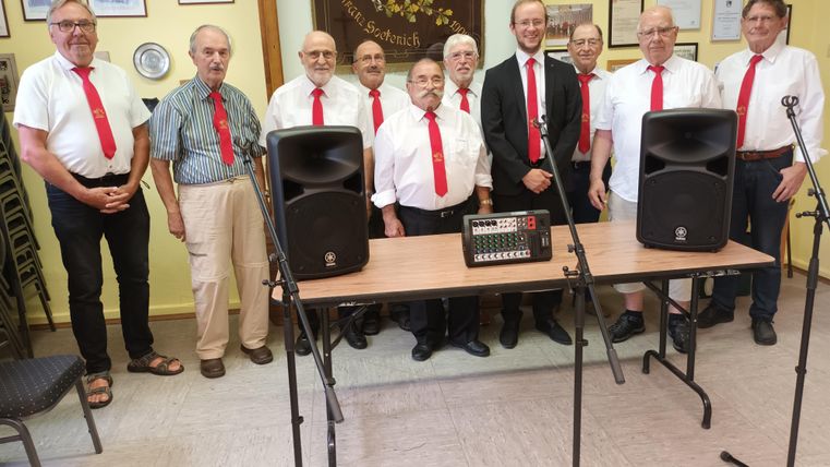 Eine große Blaskapelle steht im Freien und posiert für ein Gruppenfoto. Die Musiker tragen farbige Uniformen und halten ihre Instrumente.