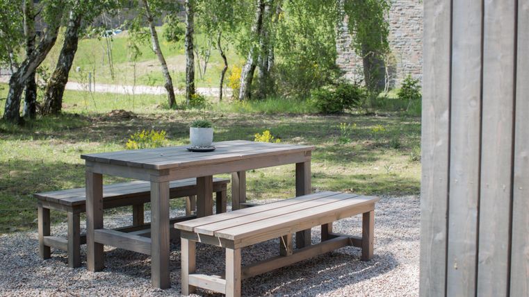 Ein schöner Esstisch aus Holz mit Bänken in einem grünen Garten. Die Umgebung ist ruhig und einladend.