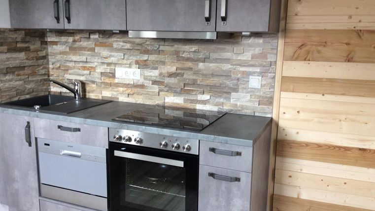 Eine moderne Küche mit grauen Schränken und einem Backofen. Die Wand ist mit Steinfliesen und Holzverkleidung gestaltet.