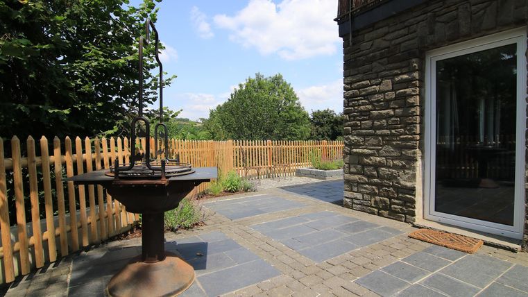 Ein schöner Außenbereich mit Natursteinboden und einem Brunnen. Im Hintergrund sind Bäume und ein Holzzaun zu sehen.