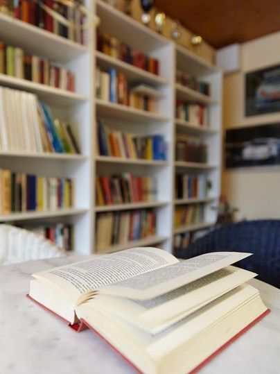 Ein aufgeschlagenes Buch liegt auf einem Tisch. Im Hintergrund sind Regale mit vielen bunten Büchern sichtbar.