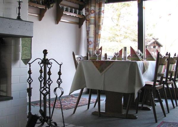 Ein gemütliches Restaurant mit einem Tisch, der für Gäste gedeckt ist. Im Hintergrund sind Stühle und ein Kamin zu sehen.