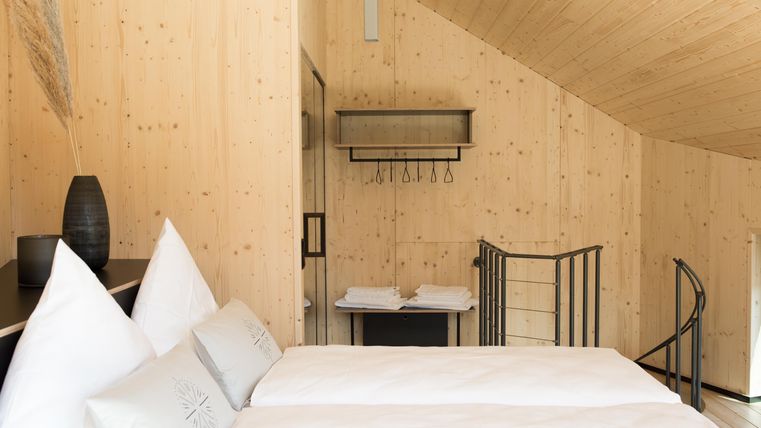 Ein modernes Schlafzimmer mit hellen Holzwänden und einem gemütlichen Doppelbett. Die Einrichtung ist schlicht und stilvoll, mit einem Blick auf eine Wendeltreppe.