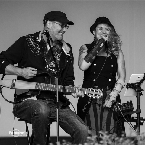 Ein Duo tritt auf einer Bühne auf. Die Musikerin singt, während der Musiker Gitarre spielt.
