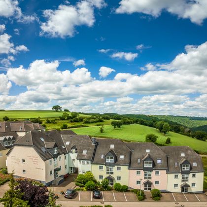 Ein modernes Wohngebäude in einer ländlichen Umgebung mit grünen Wiesen und einem blauen Himmel. Leichte Wolken ziehen am Himmel vorbei.