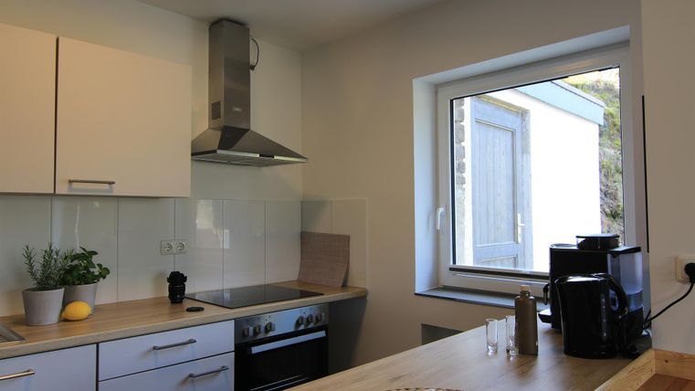 Eine moderne Küche mit weißen Schränken und modernen Geräten. Das große Fenster bietet viel Tageslicht und einen Blick nach draußen.